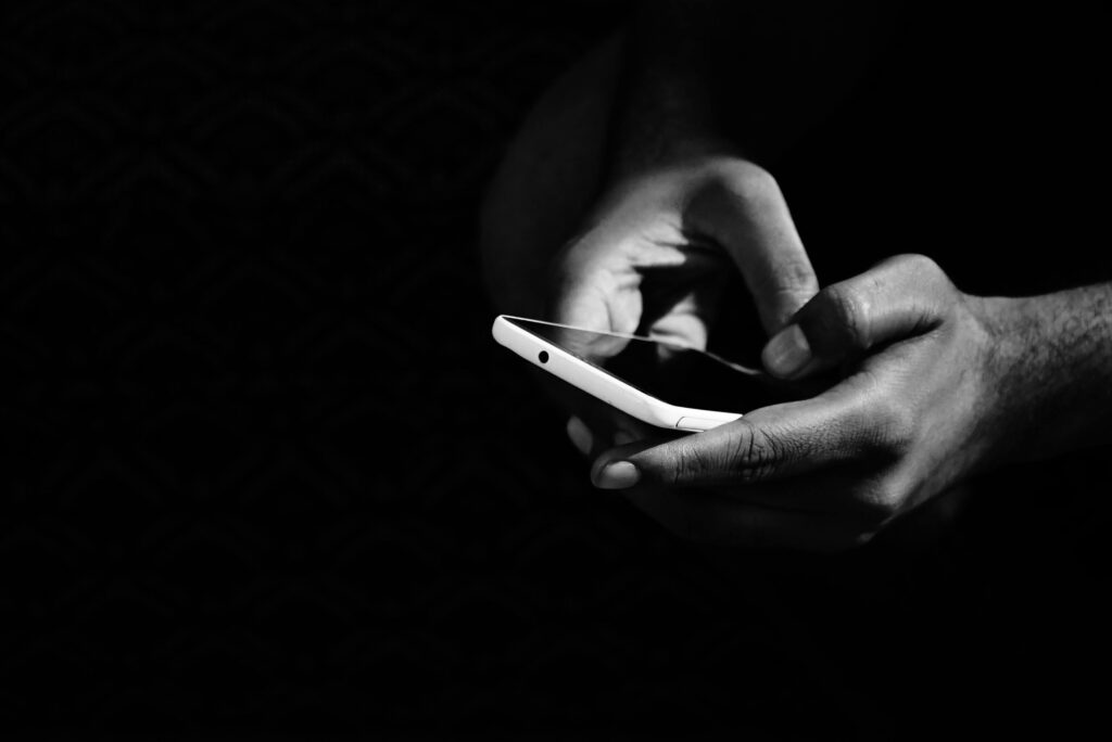 Black and white photo of hands holding a smartphone against dark background.