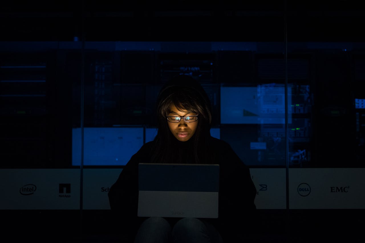 A woman deeply engrossed in programming on a laptop at night in a data center.