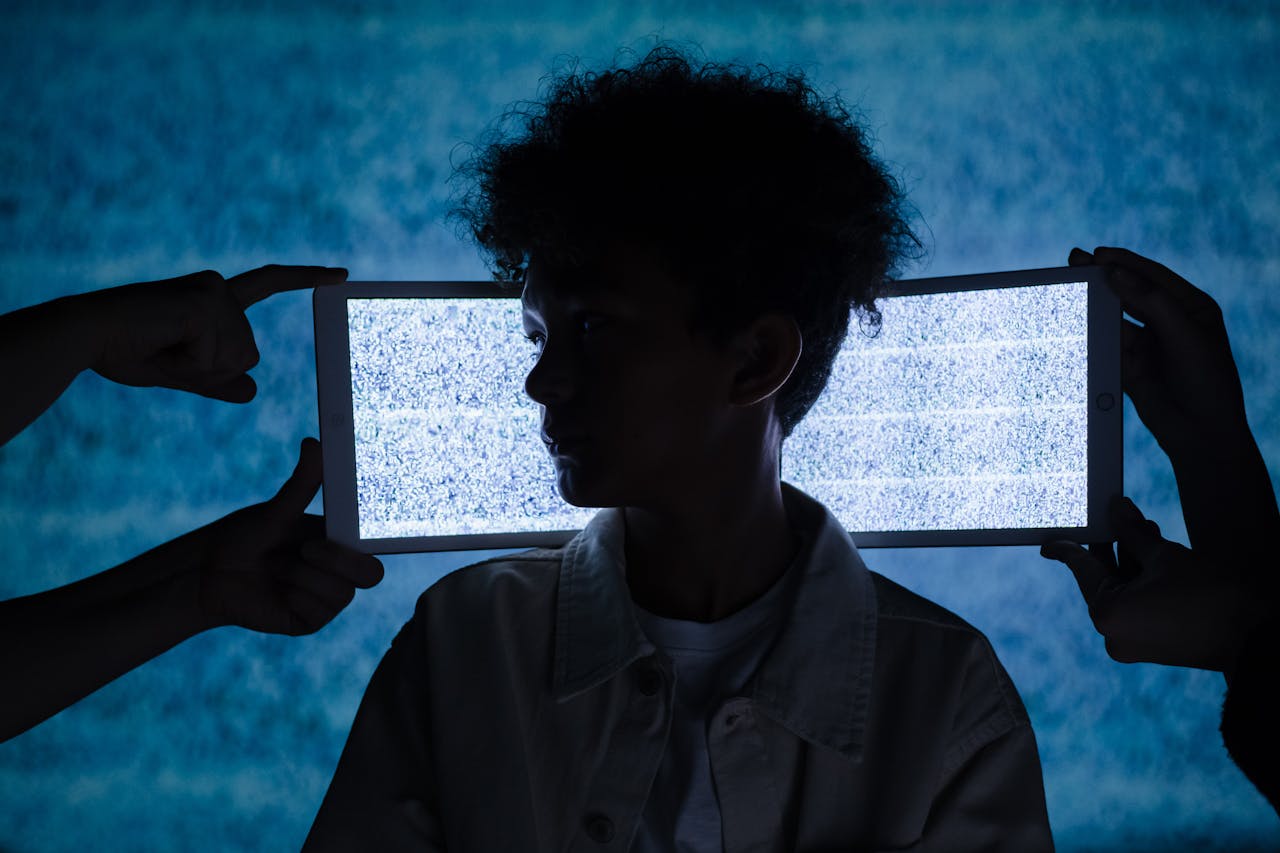 Artistic photo of a child's silhouette framed by digital tablets showing static, exploring technology and isolation.